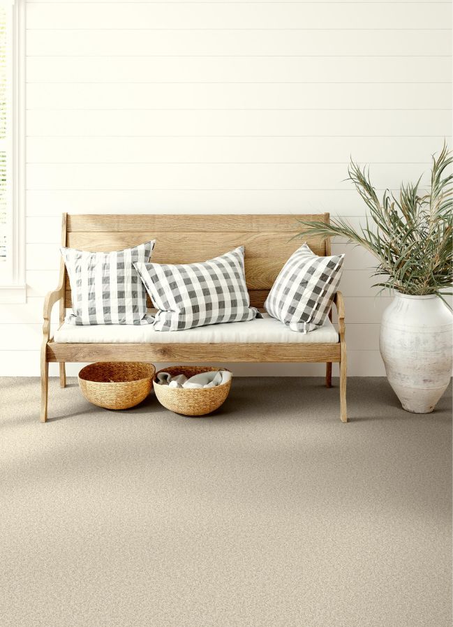 textured beige carpets in an entryway with a wood bench